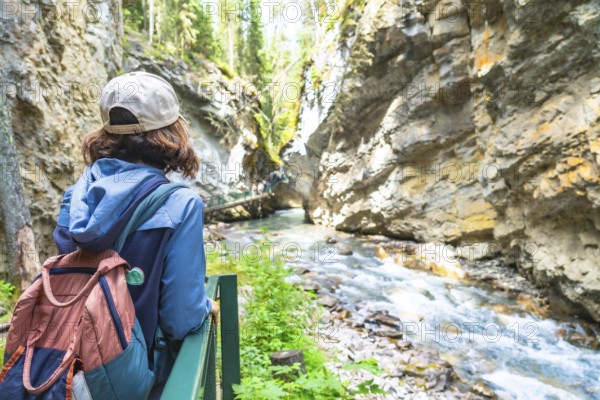 Female tourist with a backpack admiring the breathtaking turquoise waters flowing through the rocky gorge of johnston canyon in banff national park on a sunny summer day