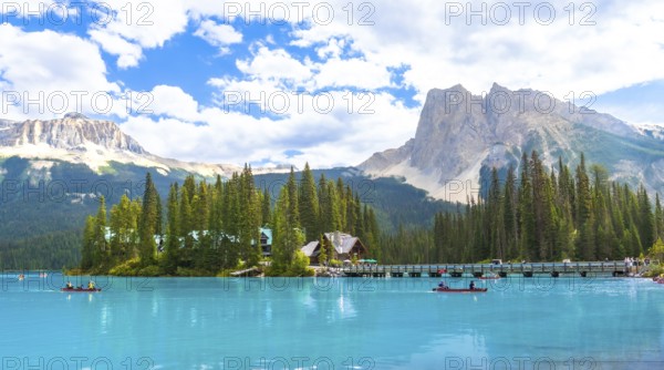 Canoeing tourists glide across the turquoise waters of emerald lake, framed by a wooden bridge, lush forest, and snow capped mountains in banff national park