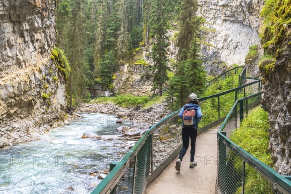 Female tourist with a backpack walking along a metal catwalk, taking in the scenic views of johnston canyon and the turquoise bow river in banff national park, alberta
