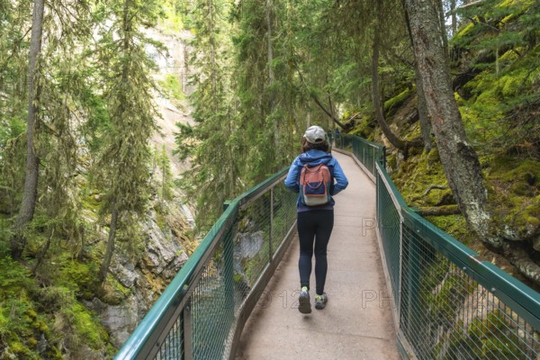 Female tourist with backpack walking on the johnston canyon catwalk trail in banff national park, alberta, enjoying the beautiful view of the canyon and forest