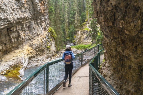 Female tourist with backpack walking on a metal catwalk enjoying the scenic view of johnston canyon and the bow river in banff national park, alberta, canada, during summer