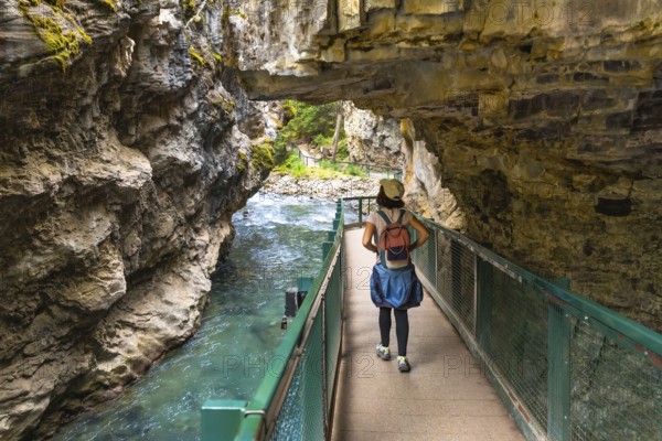 Female tourist with backpack walking on a metal catwalk built into the side of johnston canyon, with the turquoise waters of the bow river flowing below, in banff national park, alberta, canada