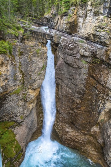 Cascading waterfall pouring into a vibrant turquoise pool amidst the rugged johnston canyon in banff national park, revealing the raw beauty of nature