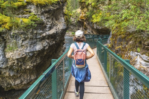 Female tourist with backpack walking on metal catwalk enjoying the view of johnston canyon and the bow river in banff national park, canadian rockies, alberta, canada, during summer