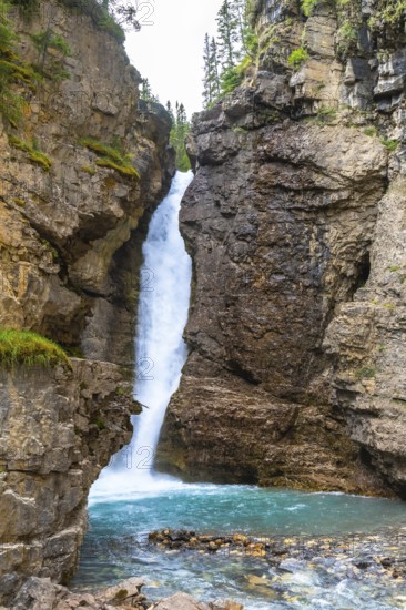 Breathtaking waterfall cascading into a vibrant turquoise pool, surrounded by rugged cliffs and lush greenery in johnston canyon, banff national park, alberta