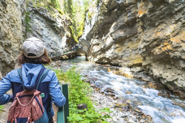 Female tourist with a backpack admiring the turquoise waters of bow river flowing through johnston canyon in banff national park on a summer day