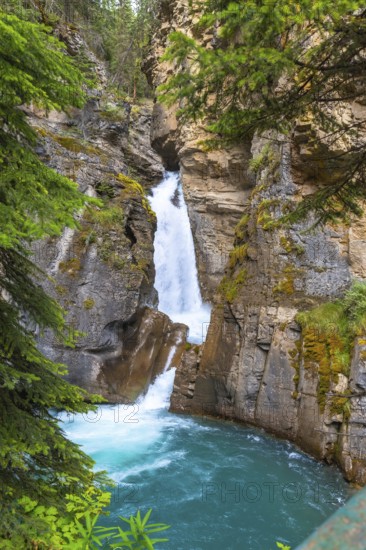 Turquoise water flows through johnston canyon in banff national park, alberta, canada, creating a picturesque waterfall cascading into a vibrant pool surrounded by lush greenery and rocky cliffs
