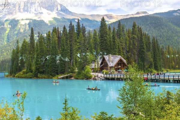 Tourists are canoeing on the turquoise waters of emerald lake with a beautiful wooden lodge and the canadian rockies in the background, in banff national park, alberta, canada
