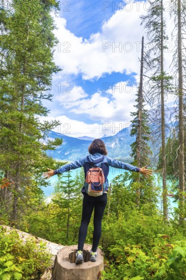 Female hiker standing on a tree stump with outstretched arms enjoying the breathtaking view of turquoise emerald lake and surrounding mountains in banff national park. Alberta. Canada. On a sunny day