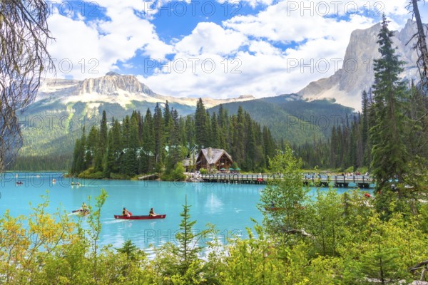 Canoeing tourists navigate the turquoise waters of emerald lake, with a wooden lodge and bridge set against the breathtaking canadian rockies in banff national park on a sunny summer day