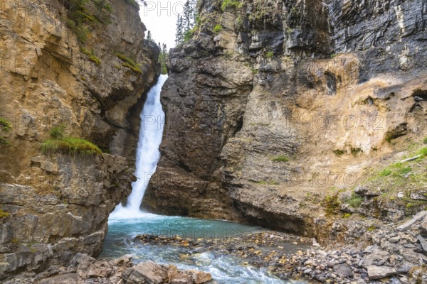 Cascading waterfall flowing into a vibrant turquoise pool in johnston canyon, surrounded by rugged cliffs and lush greenery in banff national park