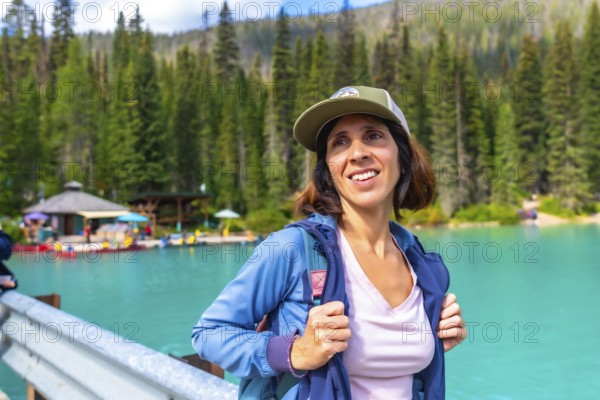 Female hiker wearing a baseball cap and backpack standing near the turquoise waters of emerald lake, admiring the scenic beauty of yoho national park in the canadian rockies, british columbia