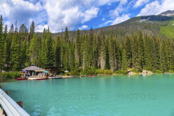 Emerald lake lodge and surrounding pine trees reflecting in the turquoise waters of emerald lake, with tourists canoeing and kayaking on a sunny summer day