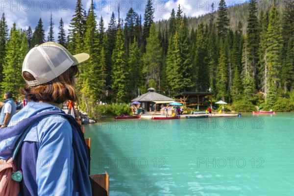 Tourist standing on a bridge admires the turquoise waters of emerald lake, surrounded by lush forests and a boat dock in banff national park, a breathtaking natural wonder in the canadian rockies