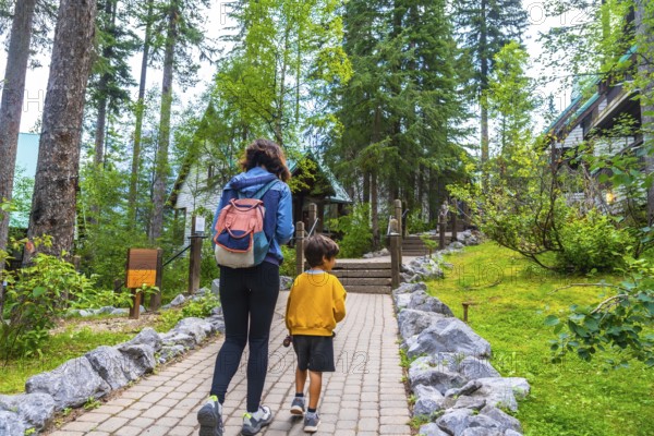 Tourists walking on a paved path approaching emerald lake lodge, surrounded by lush forest and rocky terrain, in yoho national park, british columbia, canada