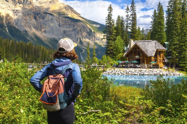 Tourist with a backpack is enjoying the breathtaking view of emerald lake and its charming wooden lodge nestled amidst the stunning canadian rockies in banff national park, alberta