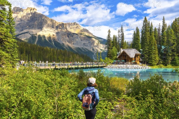 Female tourist with a backpack admiring breathtaking turquoise waters of emerald lake, featuring an iconic wooden chalet and bridge in the stunning canadian rockies