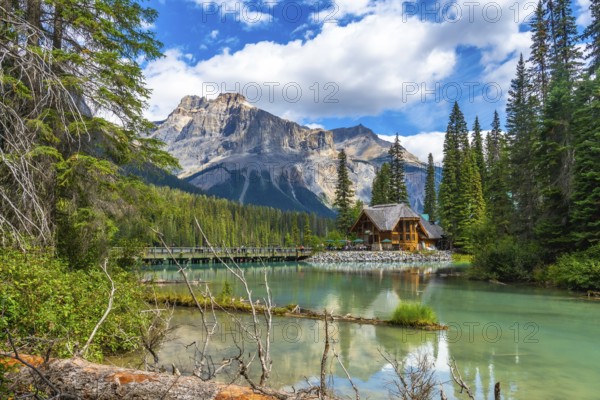 Wooden lodge reflecting in turquoise water with president range mountains towering behind and tourists walking on bridge on sunny summer day in yoho national park, british columbia, canada