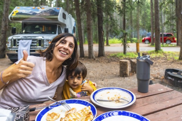 Mother and child showing thumbs up while having lunch at their campsite in banff national park, canadian rockies, with their campervan in the background