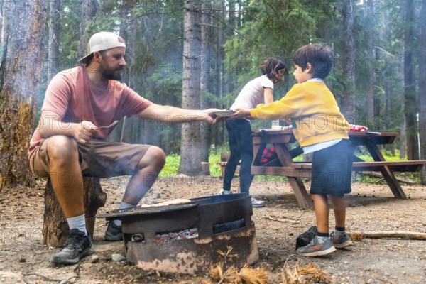 Father serving food to children at campsite, cooking on campfire in banff national park, canadian rockies, alberta, enjoying outdoor lifestyle during summer vacation