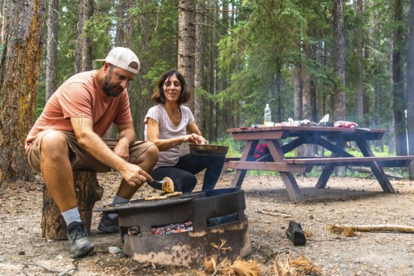 Tourists are grilling food for lunch over a campfire in a campsite in banff national park, canadian rockies, alberta, with a picnic table in the background