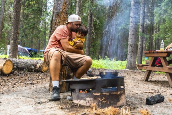 Father showing affection to his son while cooking breakfast on campfire during a camping trip in banff national park, canadian rockies, alberta