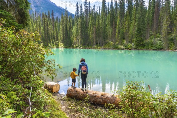 Mother and son holding hands on a log, enjoying the stunning turquoise waters of emerald lake, surrounded by lush forests and mountain peaks in banff national park