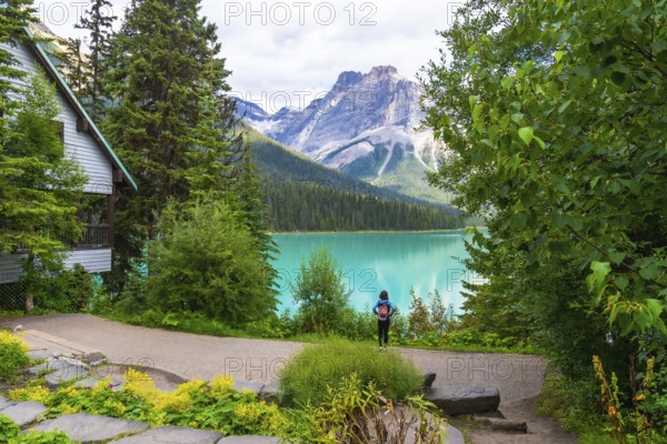 Tourist with a backpack is enjoying the breathtaking view of the turquoise waters of emerald lake, surrounded by lush forests and the majestic canadian rockies in banff national park, alberta