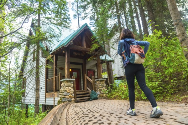 Female tourist with backpack walking on a paved path. Admiring a wooden cabin in the forest near emerald lake in banff national park. Yoho national park. British columbia. Canada. During a summer day