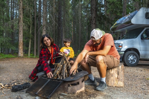 Family with little boy making campfire near their campervan during their vacation camping in the forest of banff national park, canadian rockies, alberta, canada