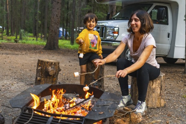 Mother and son roasting marshmallows over a campfire near their campervan in banff national park, alberta, enjoying a relaxing evening in the canadian rockies
