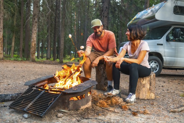 Tourists are roasting marshmallows over a campfire near their campervan in a campsite in banff national park, enjoying a relaxing evening in the canadian rockies