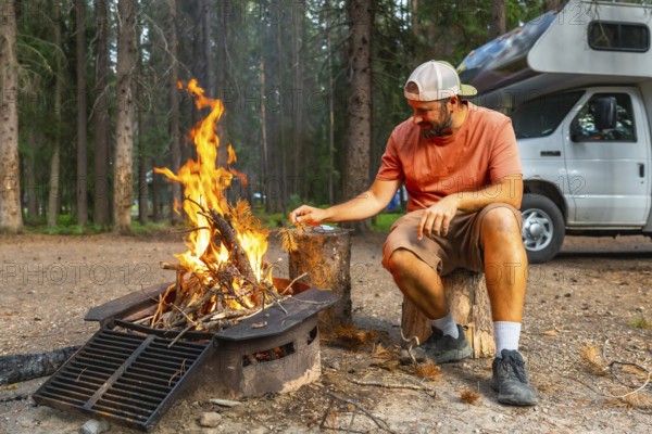 Tourist feeding campfire flames near camper van in banff national park, canadian rockies, alberta, enjoying peaceful camping experience surrounded by nature
