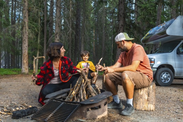 Family enjoying camping in the canadian rockies, preparing campfire next to their campervan in banff national park, alberta, during a sunny summer day