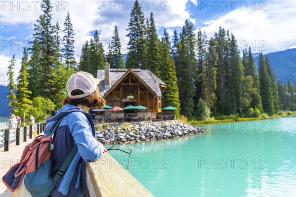 Tourist with a backpack enjoying breathtaking views of turquoise waters at emerald lake, framed by a charming wooden lodge and lush pine forest in banff national park