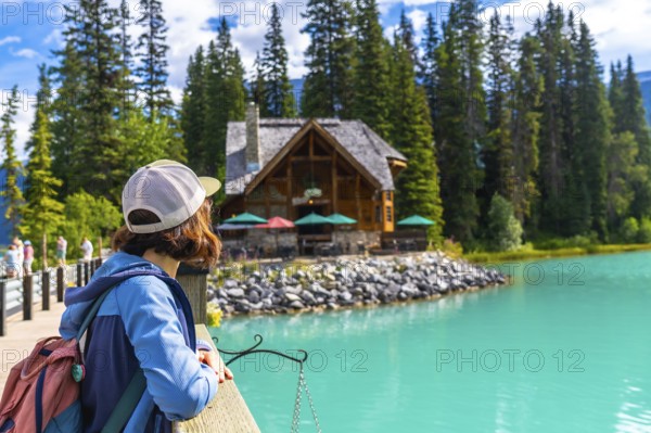 Female hiker admiring the turquoise waters of emerald lake and its charming lodge, nestled among lush pine forests in banff national park, alberta, canada