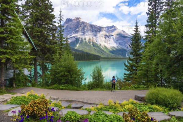 Tourist with a backpack admiring the breathtaking turquoise waters of emerald lake and the imposing mount burgess, surrounded by lush vegetation and a wooden cabin in banff national park