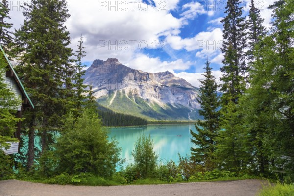 Emerald lake reflecting the majestic mount burgess under a cloudy sky, surrounded by lush vegetation and a wooden cabin in banff national park, alberta