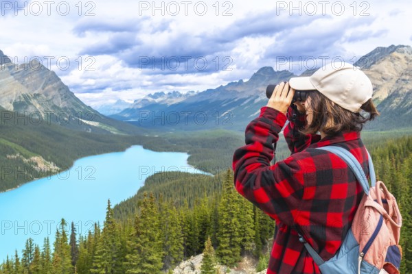 Female hiker using binoculars admires the stunning turquoise waters of peyto lake and majestic mountains in banff national park, alberta's breathtaking wilderness