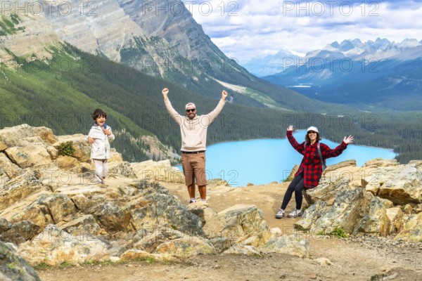 Tourists raising their arms in excitement while admiring the stunning turquoise peyto lake from a rocky viewpoint in banff national park, surrounded by majestic mountains