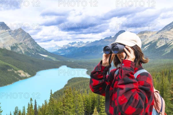 Female hiker using binoculars, admiring the scenic turquoise waters of peyto lake and the majestic mountains in banff national park, alberta, canada
