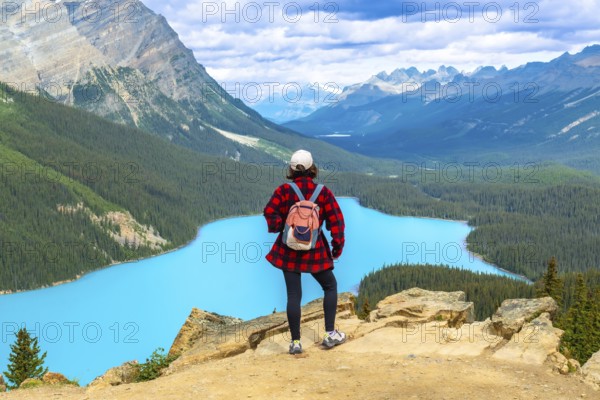 Female hiker standing on a cliff, soaking in the stunning panoramic view of turquoise peyto lake and the canadian rockies in banff national park, alberta, on a sunny day