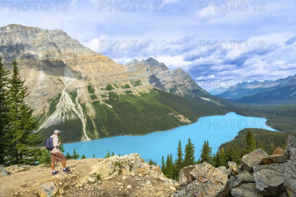 Hiker standing on a rocky outcrop, absorbing the breathtaking view of peyto lake's vibrant turquoise waters nestled in the rugged canadian rockies of banff national park