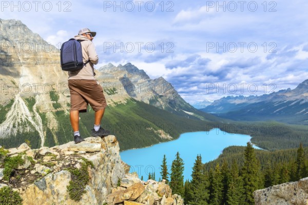Photographer standing on a rocky cliff captures a breathtaking view of turquoise peyto lake surrounded by the majestic canadian rockies in banff national park