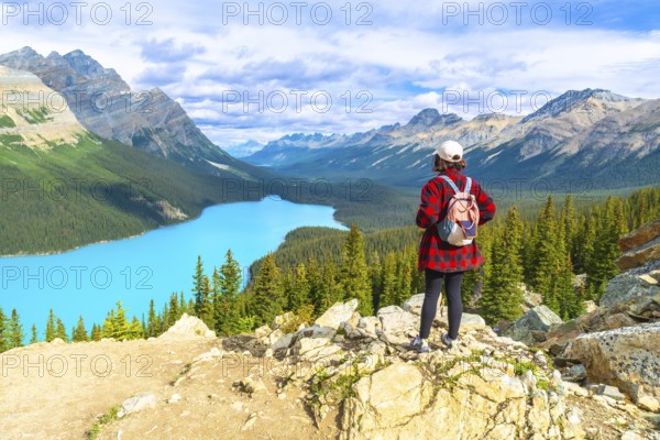 Female tourist with backpack standing on a rocky cliff overlooking the stunning turquoise waters of peyto lake and surrounding canadian rockies mountains in banff national park, alberta, canada