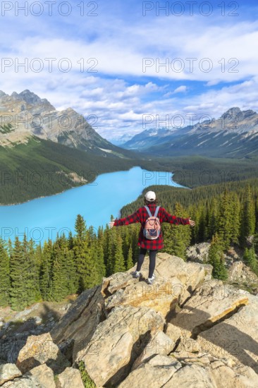 Female hiker with a backpack standing on a rocky cliff, enjoying the stunning panoramic view of turquoise peyto lake and the majestic canadian rockies in banff national park