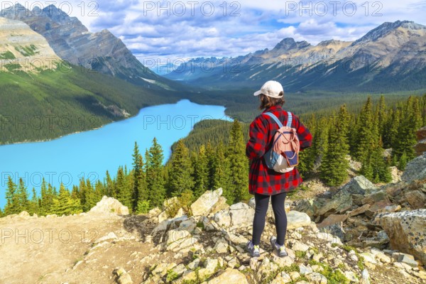 Female hiker wearing a backpack, standing on a rocky viewpoint and admiring the stunning turquoise waters of peyto lake amidst the canadian rockies in banff national park