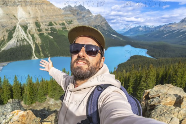 Hiker taking a selfie with outstretched arms, embracing breathtaking turquoise waters of peyto lake, surrounded by majestic mountains and lush forests in banff national park