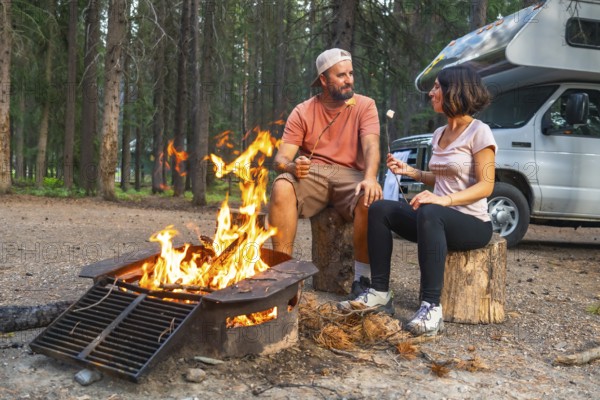 Tourists roasting marshmallows over campfire near their campervan, enjoying a peaceful evening in the wilderness of banff national park, canadian rockies, alberta