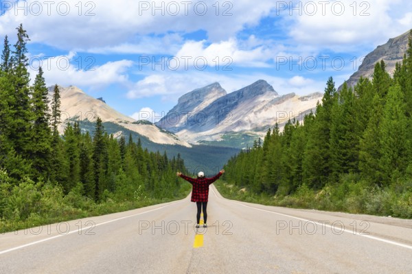 Female tourist standing on a scenic road with open arms, enjoying the freedom and breathtaking view of the canadian rockies in banff national park, alberta, under a blue sky with clouds